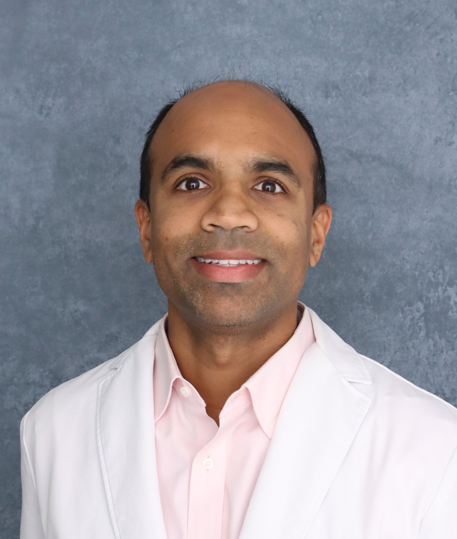 Portrait of Dr. Anand Gopalsami, wearing a white physician&rsquo;s coat, smiling at the camera.